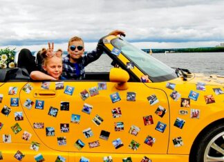 Two children driving a yellow car covered in magnets