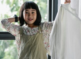 Cheerful Asian girl sorting clothes heaped on table
