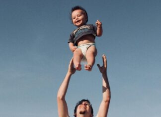 Photo of a Man Raising Baby under Blue Sky