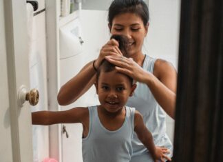 Cheerful mother doing hair of adorable daughter