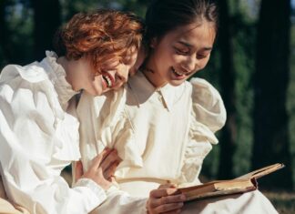 Smiling Women in Old-Fashioned Clothing Reading Book on Picnic Blanket