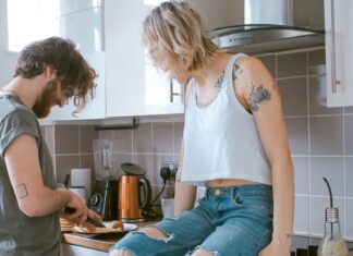 Woman sitting on counter as man chops vegetables