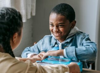 Happy black schoolboy interacting with anonymous girl during lunch
