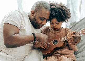 Ethnic father teaching kid playing on ukulele at home