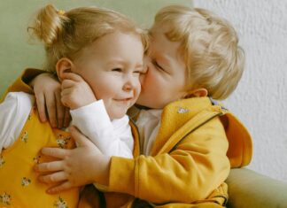 Cheerful little siblings hugging in armchair at home