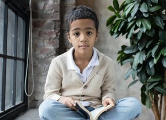 Adorable Arabian boy sitting on windowsill with opened book on knees
