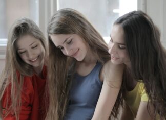 Cheerful friendly women surfing Internet on smartphone together at home