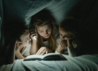 A Woman Reading a Book to her Children under a Blanket
