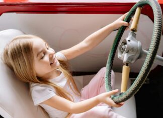 A Young Girl Sitting on the Car while Playing on Steering Wheel